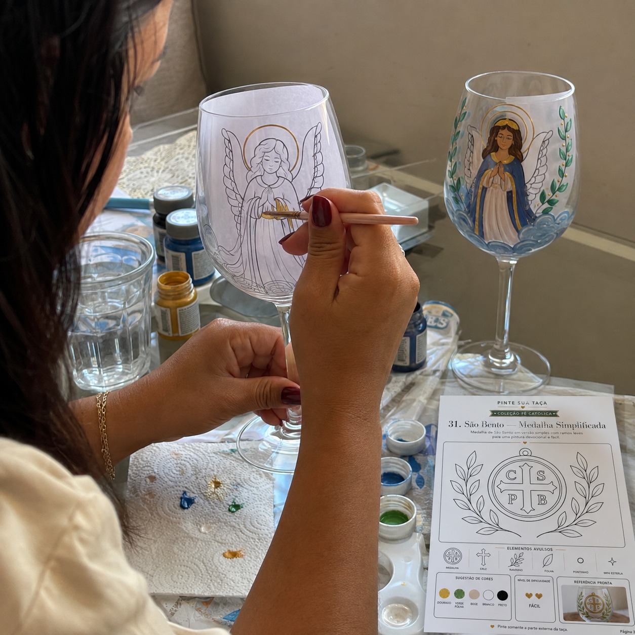 Mulher pintando taça com anjo usando o molde dentro do vidro